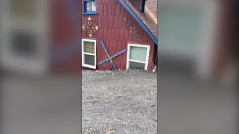 A red house is submerged by grey mud reaching its windows 