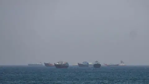 Reuters Large boats sitting about in the water close to one another. It's a hazy day and the boats on the horizon are harder to make out due to the haze 