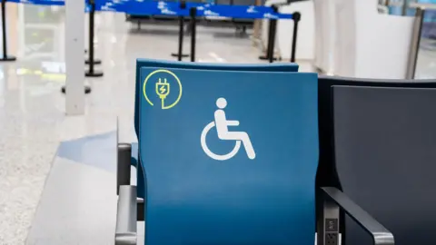Getty Images A chair with a disability sign on it it seen in an airport. Behind it, there are barriers leading up to a check in desk.