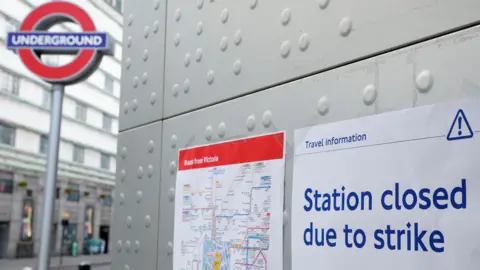  "Station closed due to strike". It is next to a bus route map and a tall Underground roundel sits in the background.