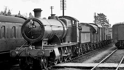 Brian England An old black and white image of the 2874 locomotive at work, with freight attached to the back