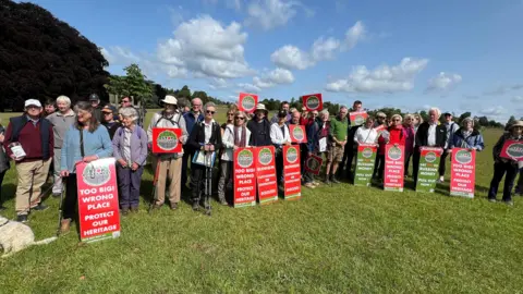 Stop Botley West campaigners standing holding red placards in a green field.