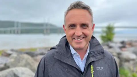 Alex Cole-Hamilton standing outside smiling, wearing a waterproof jacket. 