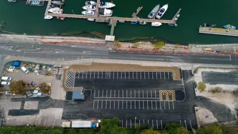 Dorset Council Aerial image of the North Quay site, which is a flat car park with parking bays outlines in white paint. Next to the car park is the sea