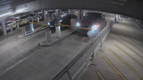 CCTV footage from Bedfordshire Fire and Rescue Service inside the car park, a red Range Rover Sport parked against the entrance barrier, a small amount of smoke coming from the engine and covering the headlights.