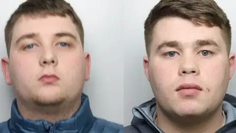 Police custody photos of two men. The man on the left has blue eyes, short hair and is wearing a blue jacket. The man on the right has green eyes, short brown hair and is wearing a blue hooded jacket.