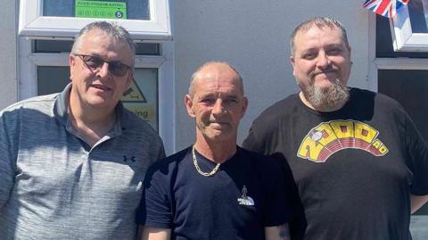Men’s Shed trustees (L-R): Dave Smith, Rob Johnstone and Richard Bradford standing outside a building in the sunshine