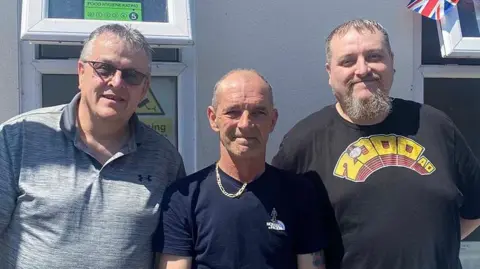 BBC Men’s Shed trustees (L-R): Dave Smith, Rob Johnstone and Richard Bradford standing outside a building in the sunshine