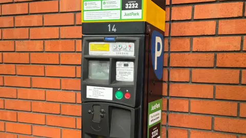 A parking meter in front of a red brick wall
