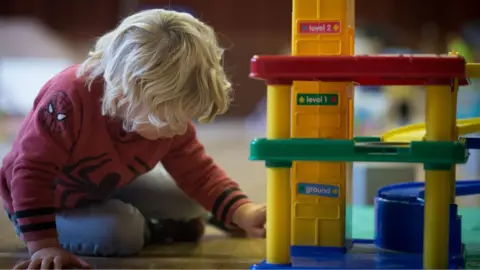 Getty Images A blond-haired child, sitting on the floor, plays with a toy multi-story cark park.