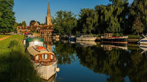 TUESDAY - Sunrise over a still river with perfect reflections of boats and a church spire against a blue sky