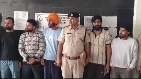 Kamal Saini A few of the deported men standing with a police official (in the centre) at Kaithal police station in India's Haryana state.