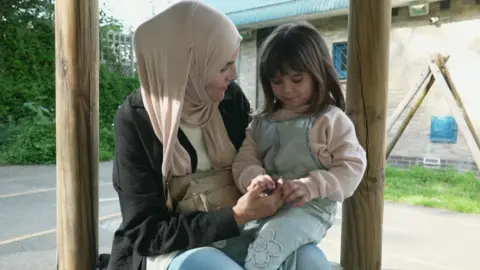 A Palestinian girl sitting on her mother's knee in a playground