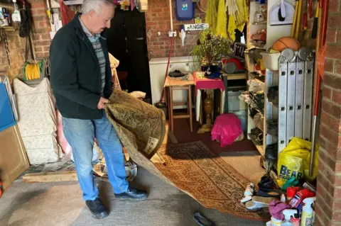 Jill Bennett/BBC Man lifting wet carpet