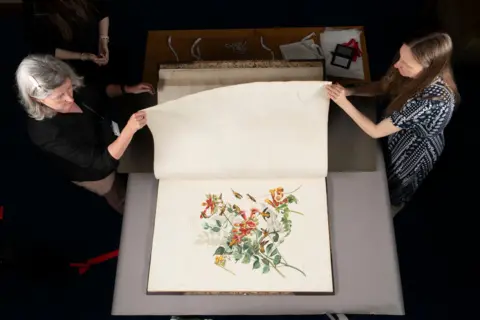 Jamie Simpson/Royal College of Physicians and Surgeons of Glasgow Claire McDade, Heritage Lead, and Clare Harrison, Library and Heritage Manager, turning the page of Audubon book.