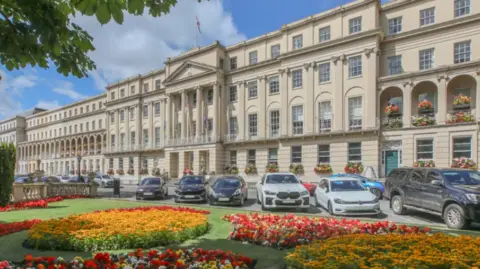 Gloucestershire Live An external view of the Regency Municipal Offices with flower arrangements in beds at the front and a row of parked cars