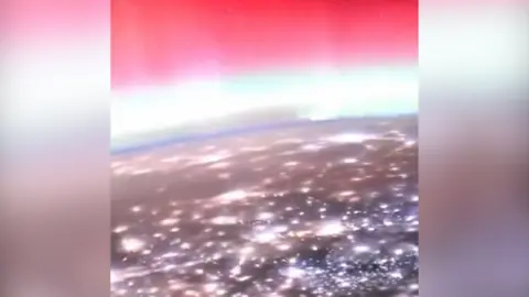 A view of lots of lights on Earth and a glowing pink sky above from the ISS