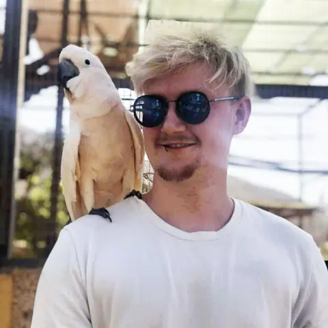 Police Scotland A man with blond hair in sunglasses and a white T-Shirt with a white parakeet on his shoulder