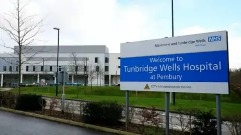A hospital sign in blue with a hospital building in the background