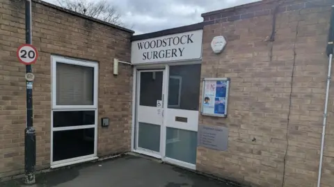 The front of Woodstock Surgery - which is a small flat roofed building on the bend of a road.