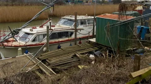 Andrew White A boat that looks abandoned on the River Hull, with broken wooden scaffolding surrounding it and broken fencing