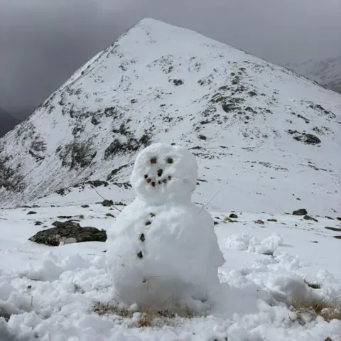 Gary Rushworth/Christopher Wallace A snowman at the foot of snow-capped hills.