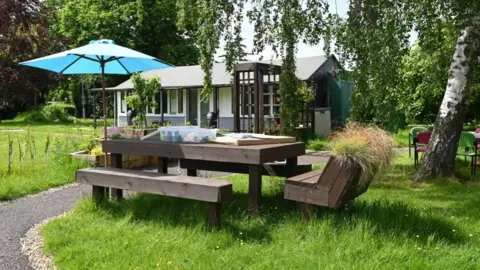 NHS Surrey and Borders Partnership A wooden table with chairs and a bench in a garden.