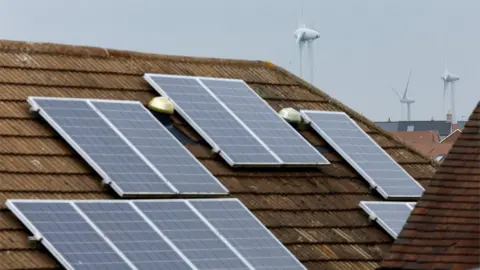 Solar panels on roof with wind turbine in the background