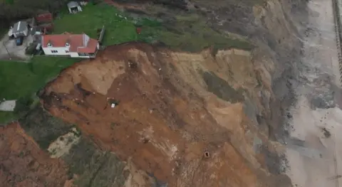 Jonny Michel/BBC A drone image of the farmhouse partially hanging over the cliff edge