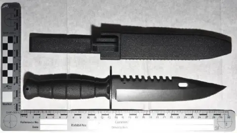 CPS A knife with a black handle and a sharp point. It has a ridged edge on part of the blade. It is next to an evidence ruler.