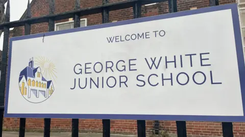 Madison Jennings/BBC The outside of a junior school. Attached to the gates is the school sign which is white with purple writing and says WELCOME TO GEORGE WHITE JUNIOR SCHOOL.