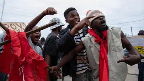 AFP Protesters shouting and pointing in Maputo. A hand-made sign can be seen in the background - Thursday 31 October 2024