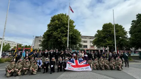 A large group of military personnel in uniform holding a Union Jack flag in Plymouth City Centre.