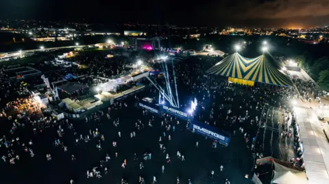 Emerge Aerial view of Emerge last year. Lots of people there. The tents and main stage are lit up and the Belfast skyline can be seen in the background.