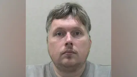 A mugshot of Ross Clancy. He has a patchy goatee and he grey hair.