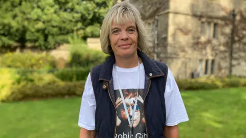 Louise James wears a dark blue gilet and a Robin Gibb t shirt.