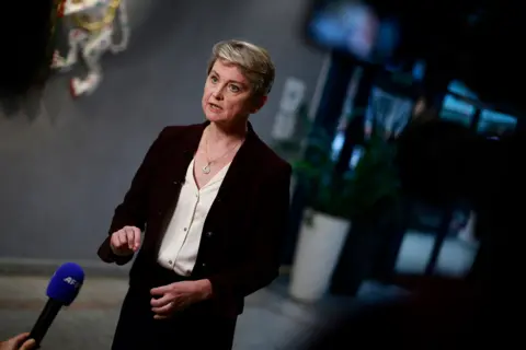 Benjamin Cremel/PA Wire Home Secretary Yvette Cooper wearing a black blazer and white blouse speaks into a microphone during a press conference 