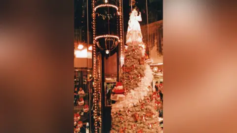 Trevor Wilson A circular shaped glass lift with lights on with Christmas decorations surrounding it.