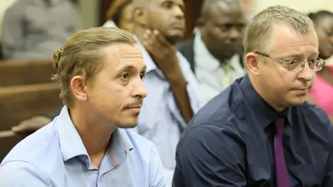 Standard Newspaper Richard and Philip Veevers sit next to each other in court. Richard, on the left, has his hair in a bun and is wearing an open kneck blue shirt. Philip sits on the right - he has short hair and glasses, he is wearing a dark blue shirt with a purple tie.
