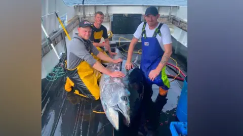 Three crew members on board The Dominator with a large bluefin tuna.