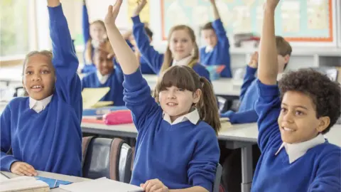 Getty Images Children in school holing their hands up