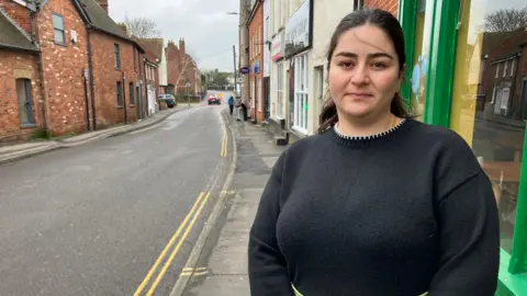 Henry Godfrey-Evans/BBC A woman wearing a dark jumper standing next to a road.