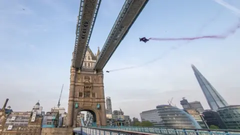 Dominik Angerer/RedBull/PA Marco Fürst and Marco Waltenspiel fly under the top section of Tower Bridge in London in their wingsuits, leaving behind red smoke trails