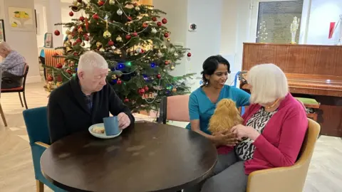 BBC A nurse sat around the table with two residents of a care home