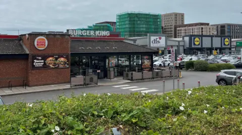 A restaurant building surrounded by seating. The building has two signs on the roof, both reading "Burger King".