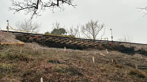 A view from below of the landslip, which shows shows the track dangling in the air and no land supporting it.