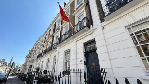 A residential two-story town house on a London street can be seen, with the door number "40", as well as the red flag of Montenegro