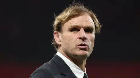 Head and shoulders view of Scott Robertson, who is wearing a white shirt with a collar and a dark suit jacket and looking slightly to his right in the direction of the camera