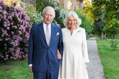 Chris Jackson/Getty Images King Charles and Camilla pose in a garden in Italy in Spring. He is wearing a blue suit and she is wearing a cream dress. They are smiling