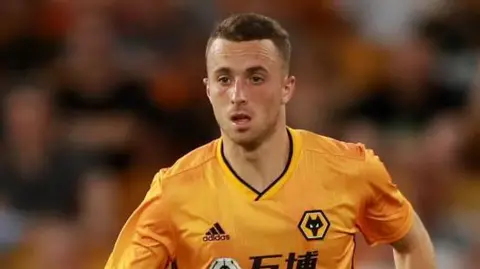 Diogo Jota wearing a Wolves shirt - back when he was a player for the club. He is running across the pitch during a game. Behind him are fans in the stadium, but the photo has blurred them.